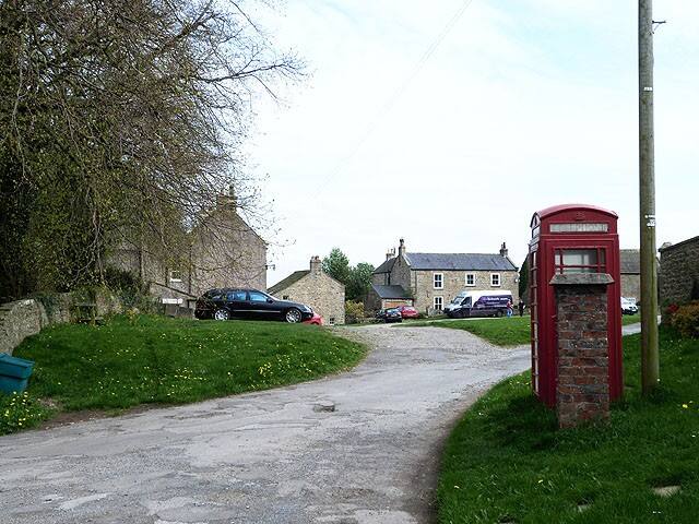 A red telephone box beside the road at Kirby Hill village green