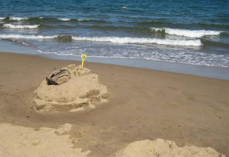 A sandcastle with a spade stuck in it at the edge of the sea
